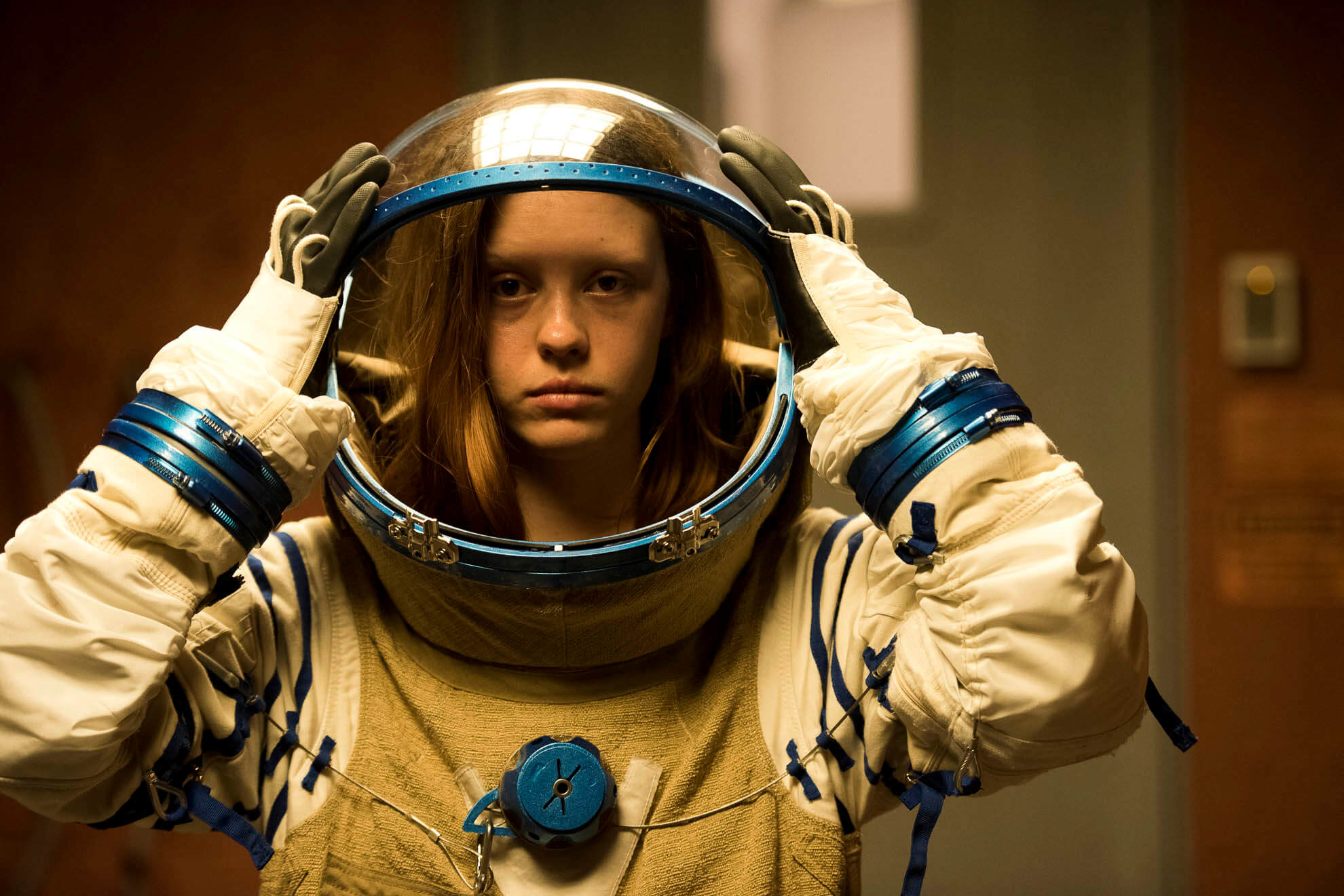 LA joven actriz Mia Goth en un fotograma de la película High Life colocándose la escafandra de un traje espacial.
