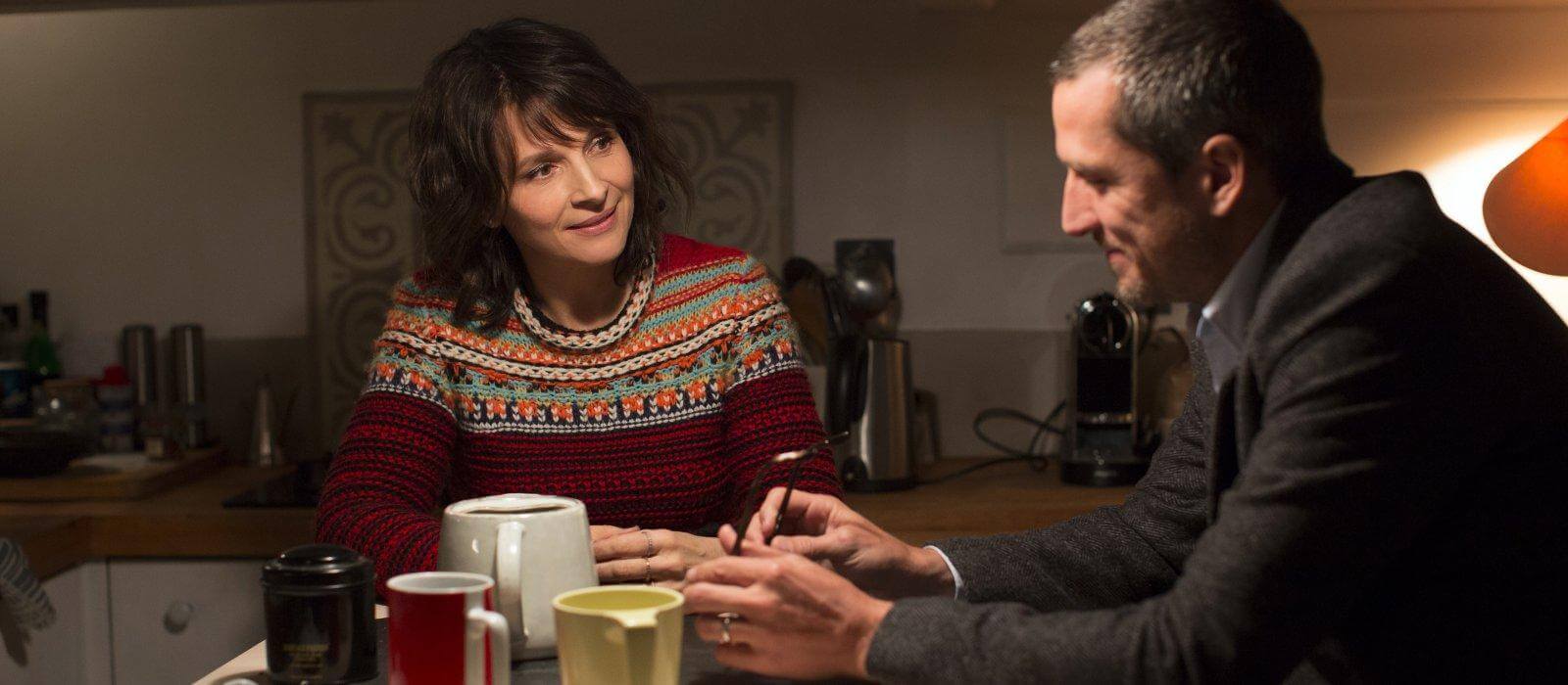 Juliette Binoche y Guillaume Canet sentados en una mesa de cocina con tazas de té sobre ella, en una escela de la película Vidas dobles de Olivier Assayas.