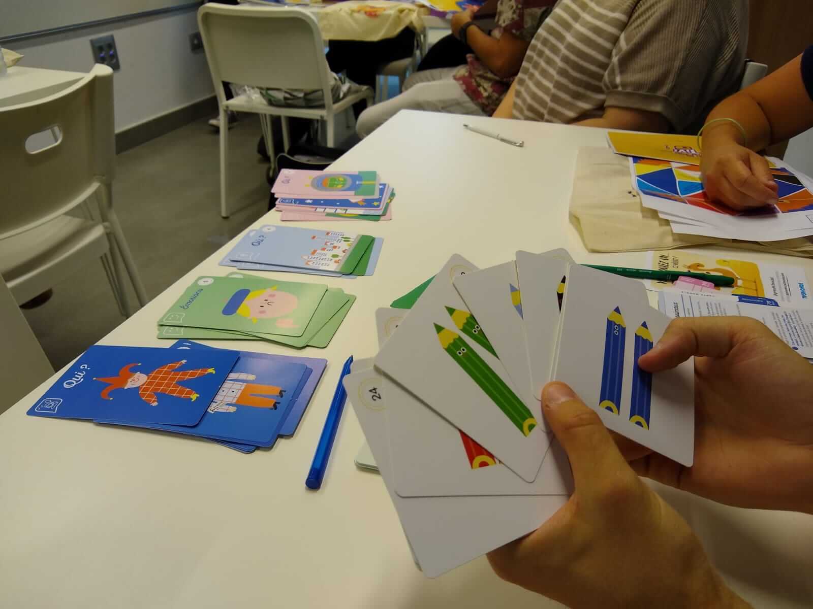 Primer plano de unas manos sobre un pupitre sosteniendo tarjetas didácticas con ilustraciones atractivas para que los niños aprendan frances. Se trata del material de una formación para profesores llevaba a cabo en la Alianza Francesa de Málaga.