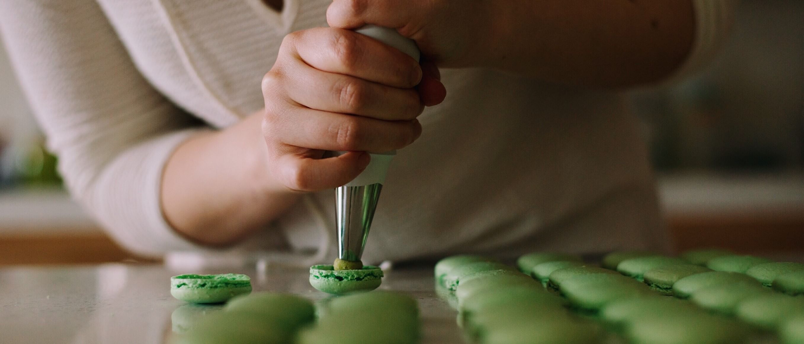 postres franceses: unas manos sosteniendo una manga pastelera rellenando macarons